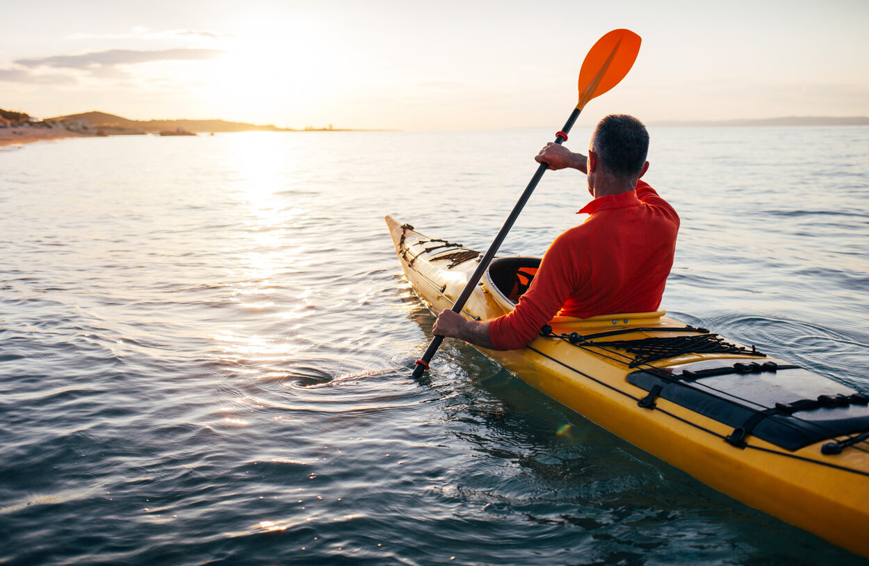 Senior man paddling kayak on the sunset sea