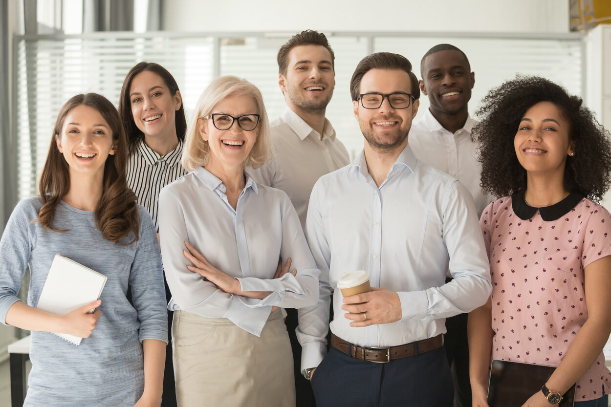 Smiling multiethnic employees standing looking at camera making team picture in office together happy diverse work group or department laugh posing for photo at workplace show unity and cooperation